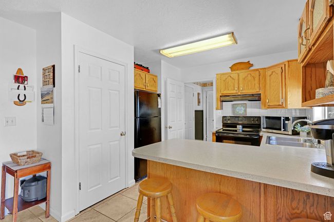 Kitchen featuring black appliances, under cabinet range hood, a peninsula, a sink, and light countertops | Image 10