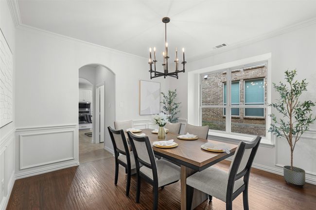 Dining room with visible vents, arched walkways, dark wood-style flooring, ornamental molding, and a notable chandelier | Image 10
