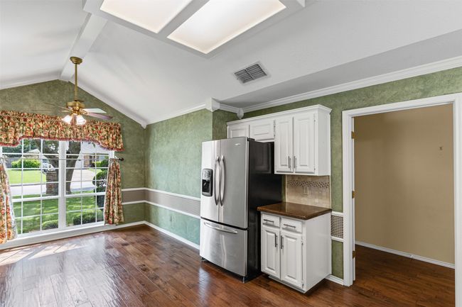 Kitchen featuring stainless steel fridge with ice dispenser, dark wood-type flooring, dark countertops, white cabinetry, and vaulted ceiling. | Image 5