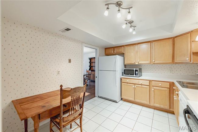 Kitchen with white appliances, wallpapered walls, a raised ceiling, light countertops, and light brown cabinetry | Image 25