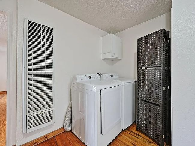 Laundry room with a heating unit, light wood-type flooring, separate washer and dryer, a textured ceiling, and cabinet space | Image 15