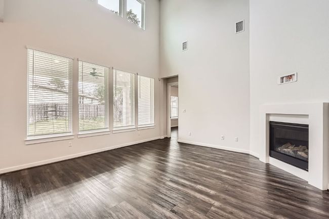 Unfurnished living room with a towering ceiling, dark wood finished floors, baseboards, and a glass covered fireplace | Image 6