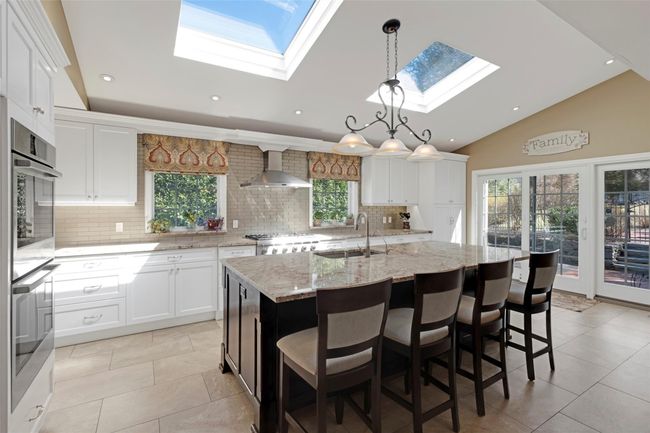 Kitchen featuring range, white cabinets, a sink, wall chimney range hood, and lofted ceiling with skylight | Image 11