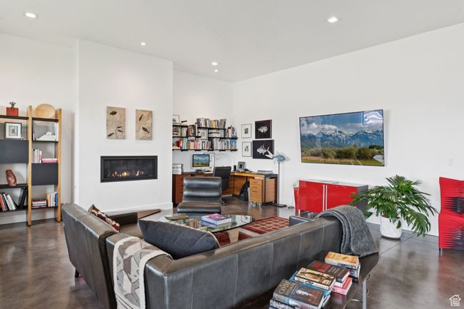 Living room with concrete floors, a glass covered fireplace, an office area, and recessed lighting | Image 56