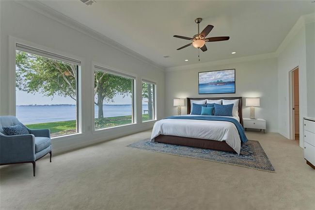 The first primary bedroom features three expansive windows offering a panoramic view of the lake. New carpet, double crown molding and neutral finishes create a custom and calming space. Photo has been virtually staged to show furniture placement. All carpet in the home is Shaw brand, comfort quiet nylon. | Image 21