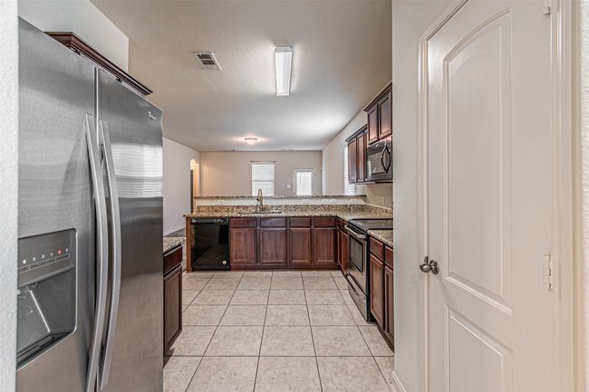 Kitchen featuring black appliances, a sink, light stone counters, a peninsula, and light tile patterned floors | Image 7