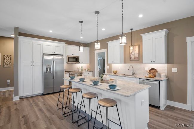 Kitchen with a kitchen bar, white cabinets, a center island, a sink, and stainless steel appliances | Image 9