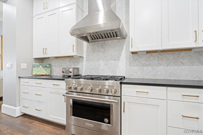 Kitchen with wall chimney exhaust hood, white cabinets, dark countertops, high end stove, and dark wood-type flooring | Image 15
