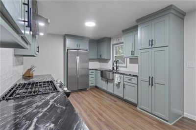 Kitchen featuring backsplash, light wood-type flooring, stainless steel refrigerator, sink, and dark stone countertops | Image 1