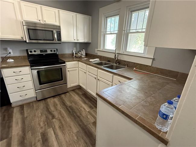 Kitchen with appliances with stainless steel finishes, a sink, white cabinetry, and dark wood-type flooring | Image 9