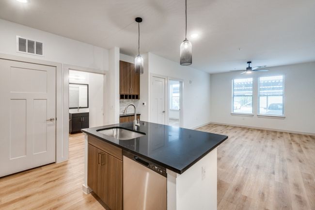 Kitchen with visible vents, a sink, stainless steel dishwasher, dark countertops, and brown cabinetry | Image 12
