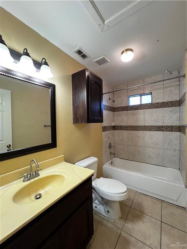 Bathroom featuring toilet, vanity, tile patterned floors, bathtub / shower combination, and a textured wall | Image 7