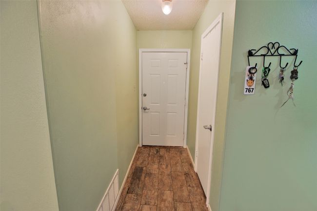 Hall featuring dark wood-type flooring, baseboards, a textured ceiling, and visible vents | Image 4