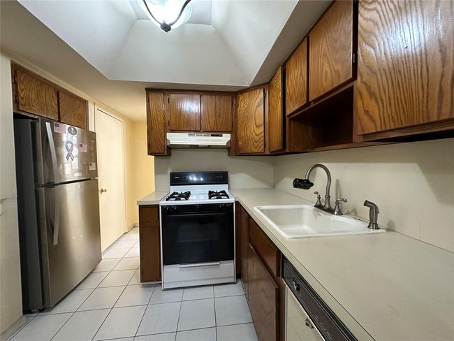 Kitchen featuring under cabinet range hood, a sink, light countertops, freestanding refrigerator, and gas stove | Image 11