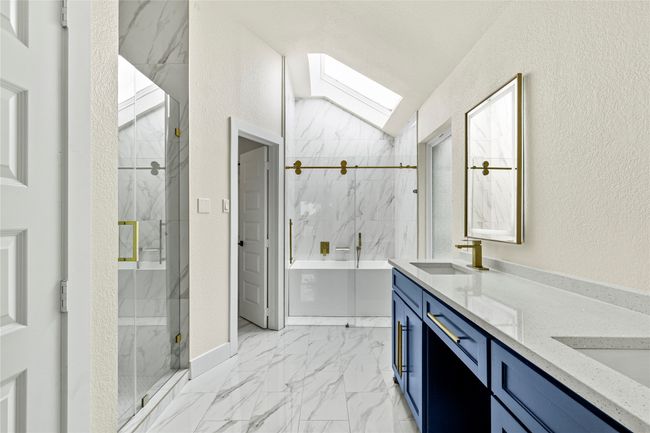 Bathroom with double vanity, a marble finish shower, a skylight, marble look tile flooring, and a textured wall | Image 20