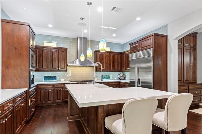 Kitchen featuring a kitchen breakfast bar, dark wood-style floors, light countertops, wall chimney range hood, and built in​​‌​​​​‌​​‌‌​‌‌​​​‌‌​​‌‌​‌​​​​​‌ appliances | Image 11