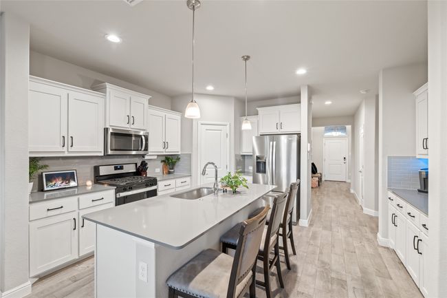 Kitchen featuring a breakfast bar area, decorative backsplash, light wood-style flooring, stainless steel appliances, and a sink | Image 4