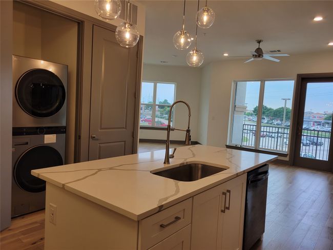 Kitchen featuring estacked washer and dryer, light wood-style floors, light stone countertops, hanging light fixtures, and ceiling fan | Image 8