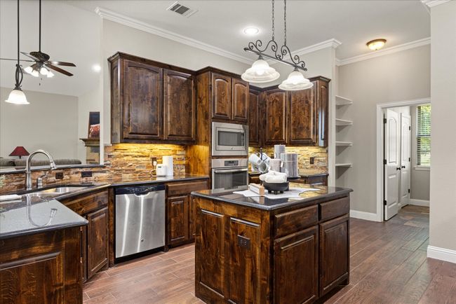 Kitchen with appliances with stainless steel finishes, a ceiling fan, decorative backsplash, dark stone countertops, and wood finished floors | Image 17