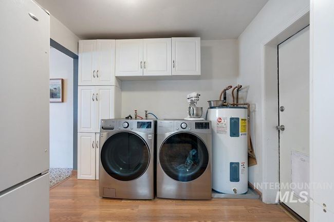 Laundry room featuring electric water heater, cabinet space, light wood finished floors, and washer and dryer | Image 15