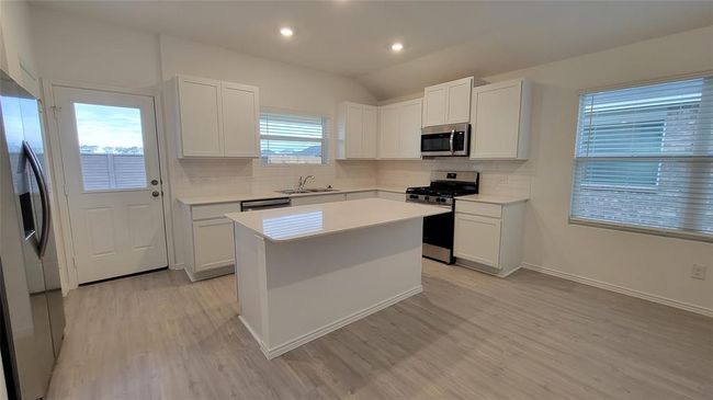 Kitchen featuring stainless steel appliances, light wood-type flooring, decorative backsplash, light countertops, and vaulted ceiling | Image 5