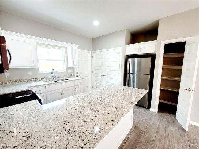 Kitchen with black range, a sink, light wood-type flooring, light stone countertops, and freestanding refrigerator | Image 7