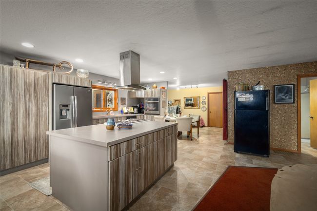 Kitchen with stainless steel appliances, island exhaust hood, a kitchen island, light countertops, and open floor plan | Image 25