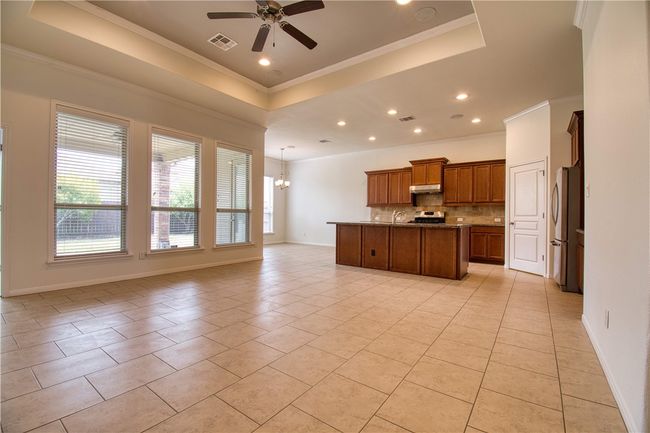 Kitchen featuring a tray ceiling, light tile patterned flooring, backsplash, open floor plan, and ceiling fan with notable chandelier | Image 10
