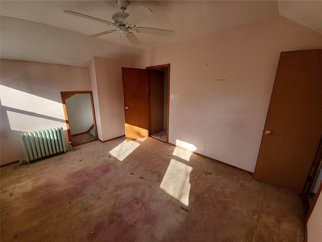 Carpeted empty room featuring radiator heating unit, ceiling fan, and lofted ceiling | Image 5