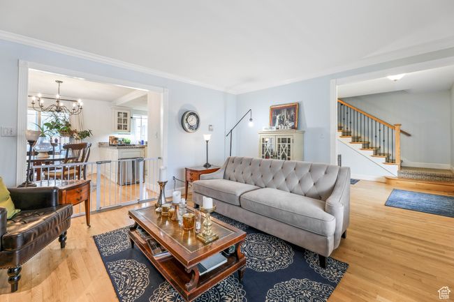 Living area with a notable chandelier, baseboards, stairway, light wood-type flooring, and crown molding | Image 5