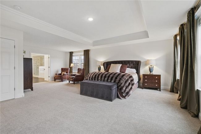 Expansive primary bedroom retreat featuring double entry doors, a tray ceiling, plush carpeting, and oversized windows that fill the room with natural light. The spacious layout offers plenty of room for a seating area or additional furniture. | Image 21