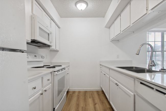 Kitchen with a sink, white appliances, light countertops, a textured ceiling, and light wood-type flooring | Image 6