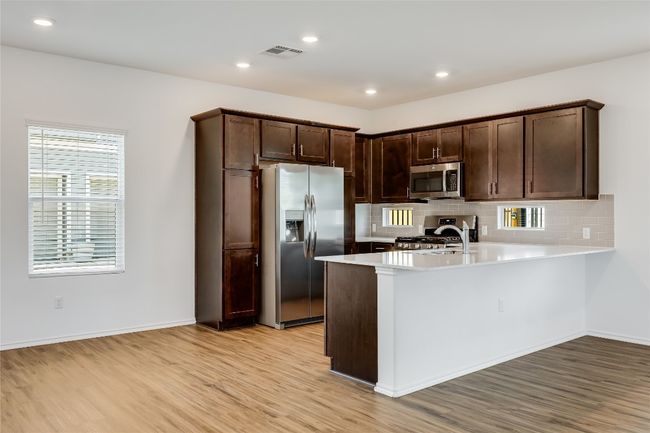 Kitchen with appliances with stainless steel finishes, light wood-style flooring, a peninsula, dark brown cabinetry, and backsplash | Image 10