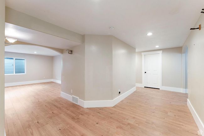 Basement hallway leading to family room with light wood-style floors, recessed lighting, and arched walkways | Image 28