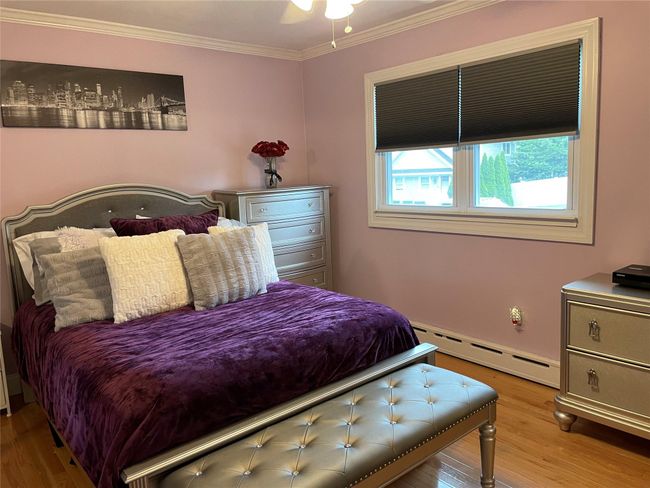 Bedroom with baseboard heating, wood finished floors, and crown molding | Image 25