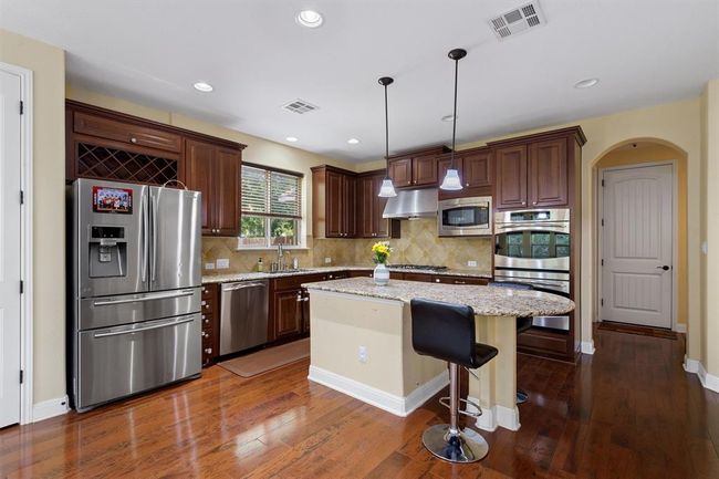 Kitchen featuring stainless steel appliances, a kitchen island, dark wood-type flooring, tasteful backsplash, and a sink | Image 12