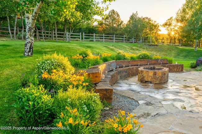 Surrounded in perennial gardens, a large stone wall and custom stone wood fire pit, this patio becomes the evening oasis for laughter and story telling. | Image 12