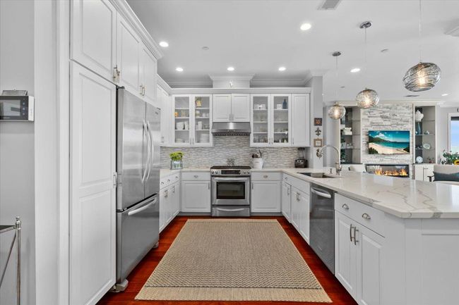 Kitchen featuring stainless steel fridge, a peninsula, visible vents, and glass insert cabinets | Image 4