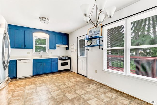 Kitchen featuring blue cabinetry, white appliances, light countertops, a chandelier, and under cabinet range hood | Image 26