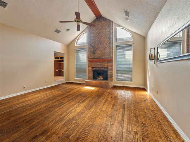 Unfurnished living room with a ceiling fan, a textured ceiling, wood finished floors, a brick fireplace, and high vaulted ceiling | Image 4
