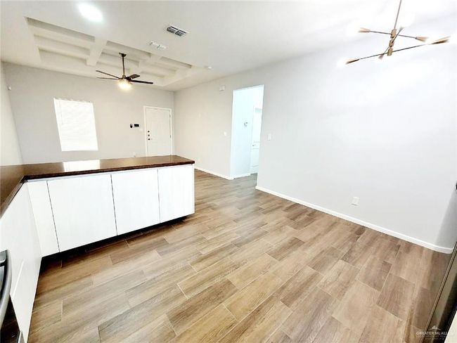 Unfurnished room featuring baseboards, light wood-style floors, visible vents, coffered ceiling, and ceiling fan with notable chandelier | Image 7