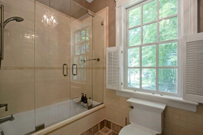 Bathroom with healthy amount of natural light, shower / bath combination with glass door, toilet, tile walls, and a chandelier | Image 25