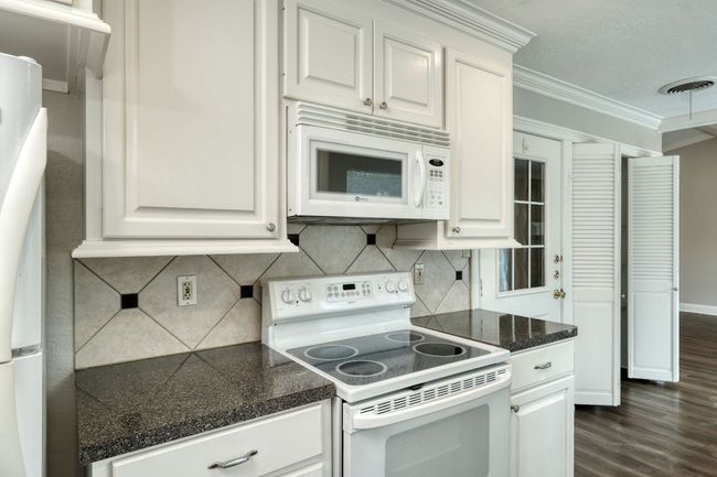 Kitchen with white appliances, ornamental molding, dark wood-type flooring, white cabinets, and backsplash | Image 5