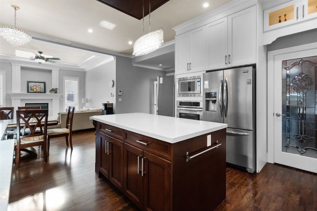 Kitchen with stainless steel appliances, light countertops, dark wood-style floors, ornamental molding, and a kitchen island | Image 12
