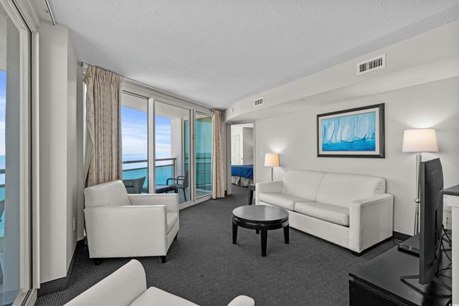 Living room with a textured ceiling, a wall of windows, visible vents, and carpet floors | Image 5