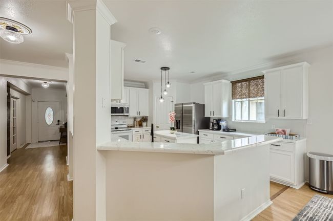 Kitchen featuring stainless steel appliances, light wood-type flooring, white cabinets, and crown molding | Image 9