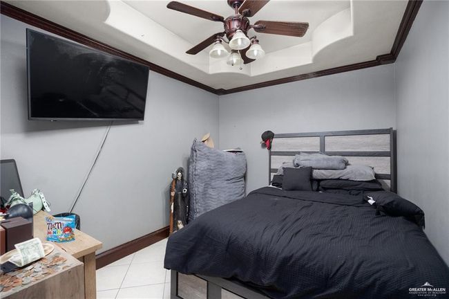 Bedroom with ceiling fan, a raised ceiling, light tile patterned floors, and crown molding | Image 15