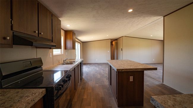 Kitchen with range with electric cooktop, under cabinet range hood, a textured ceiling, dark wood-style flooring, and a center island | Image 25