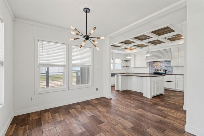 Kitchen featuring dark countertops, a kitchen island, white cabinetry, premium range hood, and coffered ceiling | Image 6