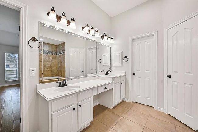 The primary bathroom features separate vanities with updated lighting, dual walk-in closets, a deep soaking tub with decorative tile surround and step-up entry, plus a spacious walk-in shower accented by coordinating mosaic tile detailing. | Image 17